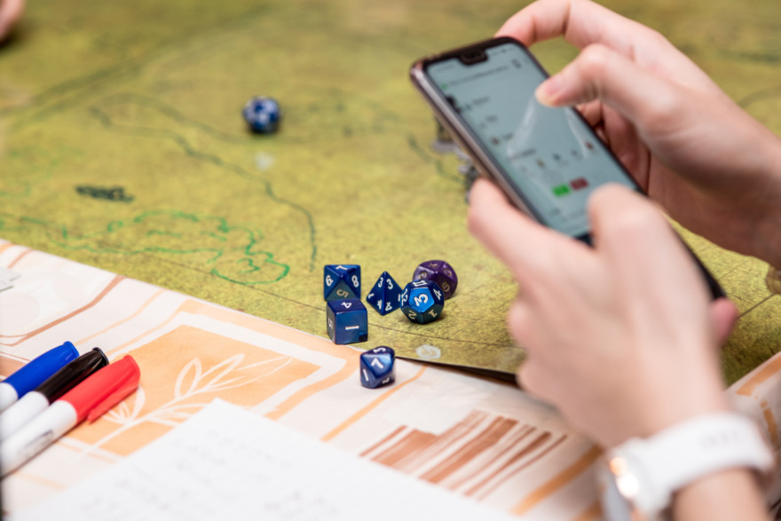 Girl Using The Smartphone During A Role Playing Game Of Dungeons And Dragons. Dices On The Green Battlefield